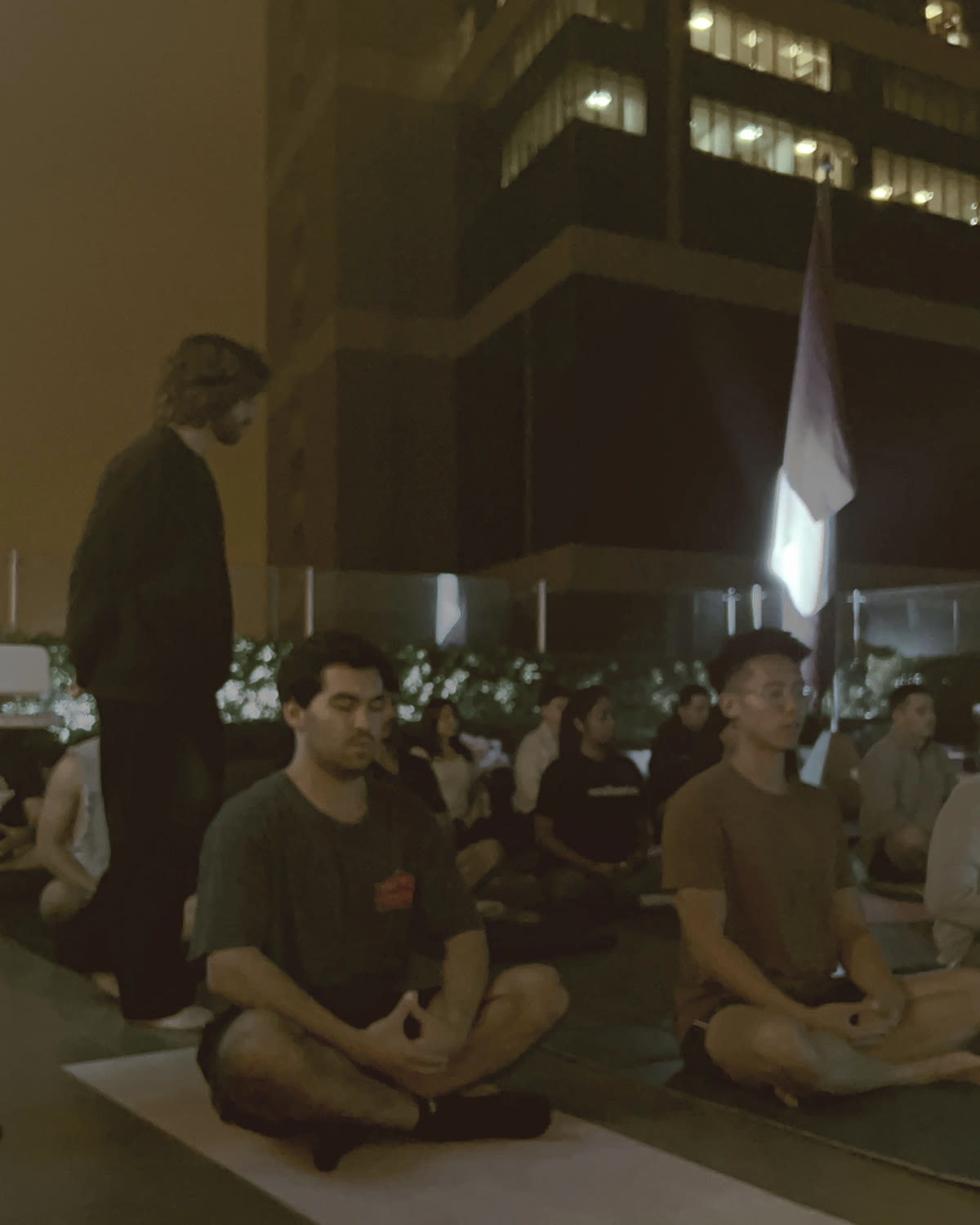 Grupo sentado meditando de noche en una terraza de oficinas, mientras Rodri guía la práctica de pie